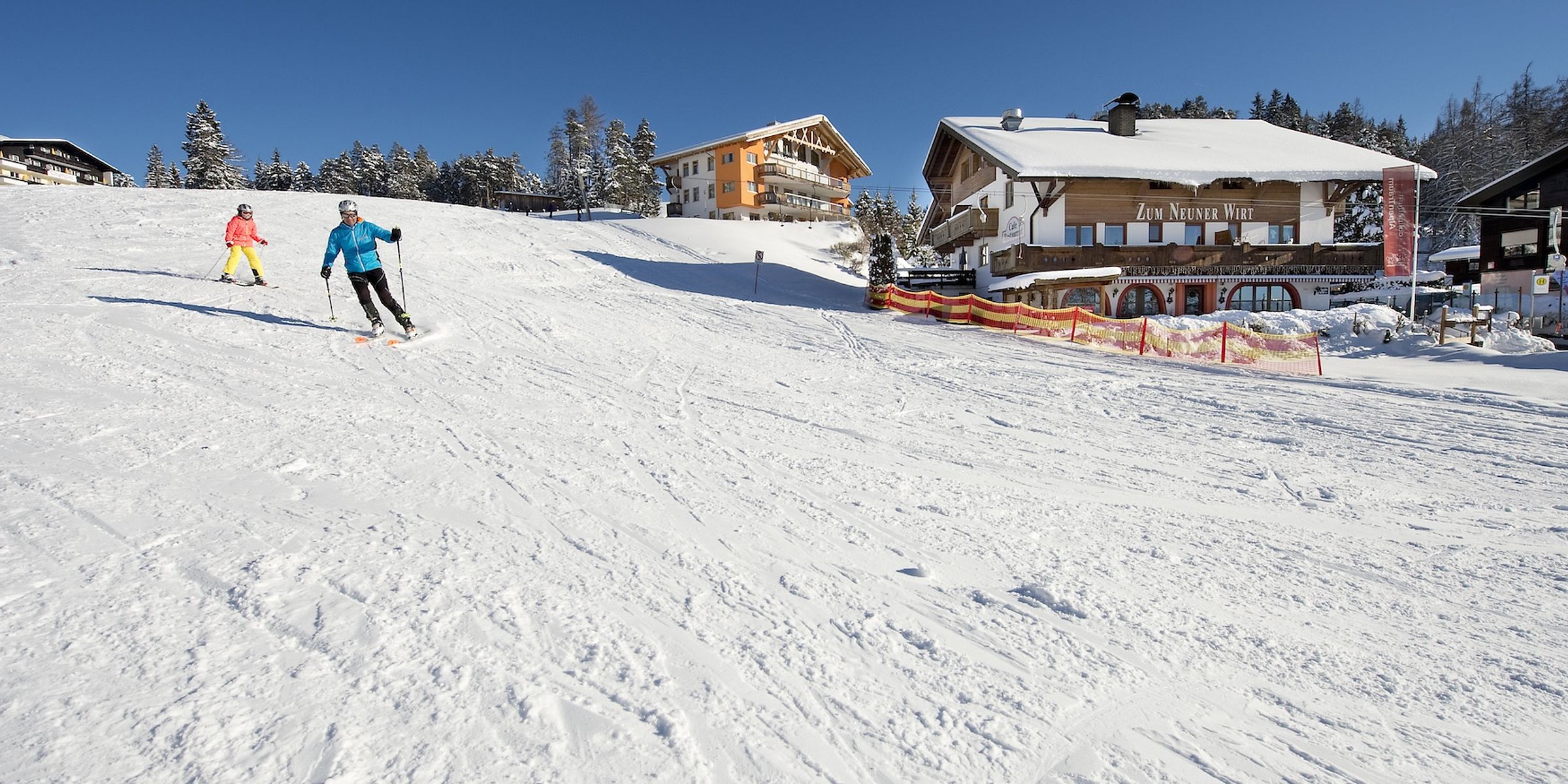 Zwei Skifahrer auf der Piste bei Mösern vor dem Gasthaus Zum Neuner Wirt